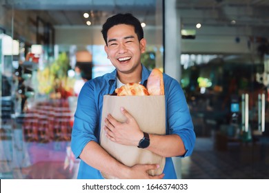 Attractive Asian Man In Blue Shirt Holding Paper Bag Shopping In Front Of Supermarket.