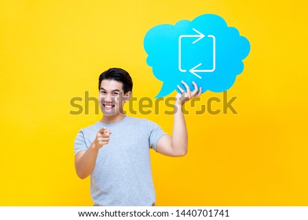 Attractive Asian man holding speech bubble with retweet sign isolated on yellow studio background