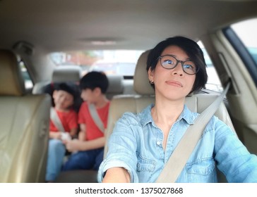 Attractive Asian Mom Driving A Car In The City With Her Kids At The Back Seat. Driving Safety Concept, Mom Lifestyle, City Life, Single Mom, Road Trip.