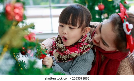 Attractive Asian Mother And Daughter Wearing Winter Outfits And Decorating Christmas Tree At Home With Joy, Preparing To Celebrate Christmas Festival. Concept For Family Christmas Party.