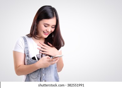 Attractive Asian teenage girl looking at her mobile phone screen with joyful face, on white background for copy space