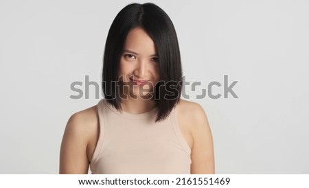 Attractive Asian woman cunningly looking at camera over gray background. Asian girl looking from under the eyebrows isolated. Smirk face