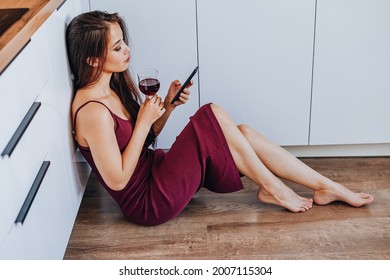 attractive Asian woman drinking wine and using a mobile phone on the floor in the kitchen of the home