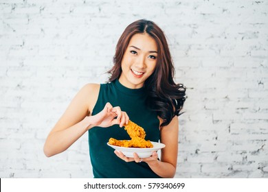 Attractive Asian Woman Eating Fried Chicken Drumstick Over White Brick Background