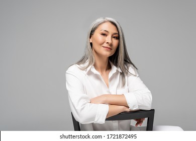 Attractive Asian Woman With Grey Hair Sitting On Chair Isolated On Grey