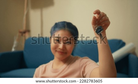 Attractive Asian woman hand holding house key smile and laugh feeling happy and exited moving in new home apartment . Young beautiful female sit on ground at living room. new home concept.