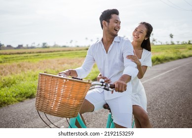 attractive asian woman with her boyfriend having fun riding a bicycle outdoor wearing white dress