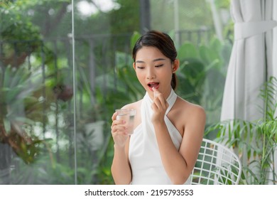 attractive asian woman holding glass of mineral water, taking pill, looking away. - Shutterstock ID 2195793553