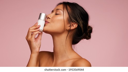 Attractive Asian Woman Kissing A Skincare Product Bottle. Female With Best Cosmetic Product For Skin.