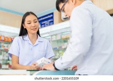 Attractive Asian Woman Pharmacist Medication Recommendation About Medicine, Drugs And Supplements To Male Patient Customer In Modern Drugstore. Medical Pharmacy And Healthcare Providers Concept.