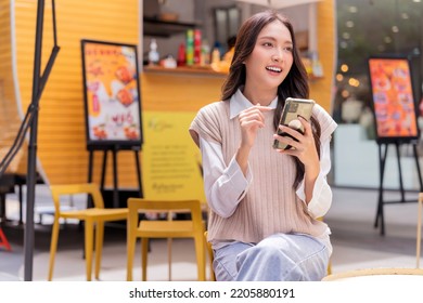 Attractive Asian Woman Pleased Positive Casual Hand Hold Smartphone Enjoy Leisure Relas Sitting In Front Of Street Food Booth Corner In Outlet Department Store Mall Relax Shopping Lifestyle Concept