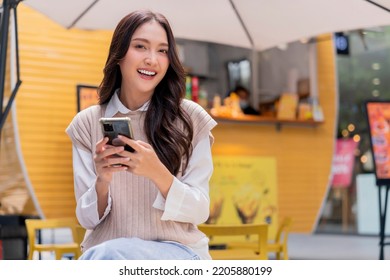 Attractive Asian Woman Pleased Positive Casual Hand Hold Smartphone Enjoy Leisure Relas Sitting In Front Of Street Food Booth Corner In Outlet Department Store Mall Relax Shopping Lifestyle Concept