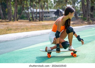 Attractive Asian Woman With Safety Skateboarding Knee Pad Skating At Skateboard Park By The Beach. Happy Female Enjoy Summer Outdoor Active Lifestyle Play Extreme Sport Surf Skate At Public Park.