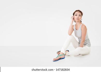 Attractive Asian woman sit on ground, full length portrait with copyspace of white wall. - Powered by Shutterstock