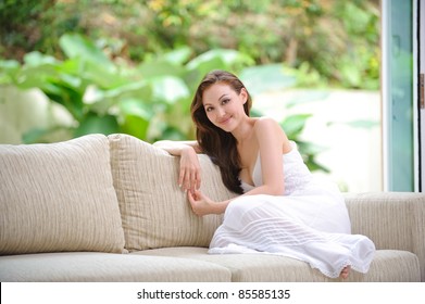 Attractive Asian woman sitting on a sofa in the living room - Powered by Shutterstock