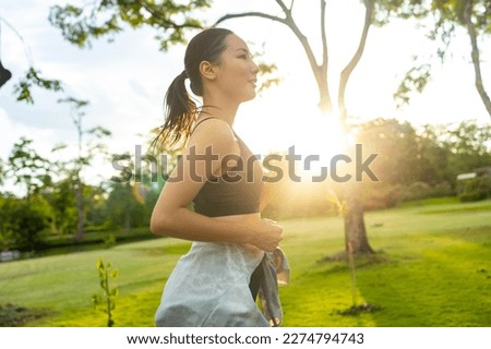Attractive Asian woman in sportswear jogging exercise at public park in summer morning. Healthy girl athlete enjoy outdoor activity lifestyle sport training fitness running workout in the city.