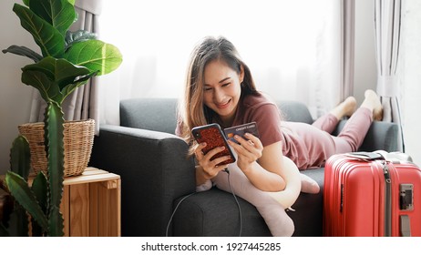 Attractive Asian woman with travel baggage have using smartphone booking flight tickets in online website and Purchase, Pay by credit card. Woman success booking travel tickets in promotion time.