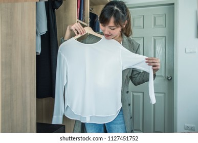 Attractive Asian  Woman Trying White Shirt In Front Of Mirror In Closet Door At Home .