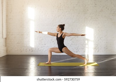 Attractive asian young woman practicing yoga asana Warrior II Pose in a training hall background. Sports shapely female in Virabhadrasana II pose during yoga class in a gym. Yoga and health concept