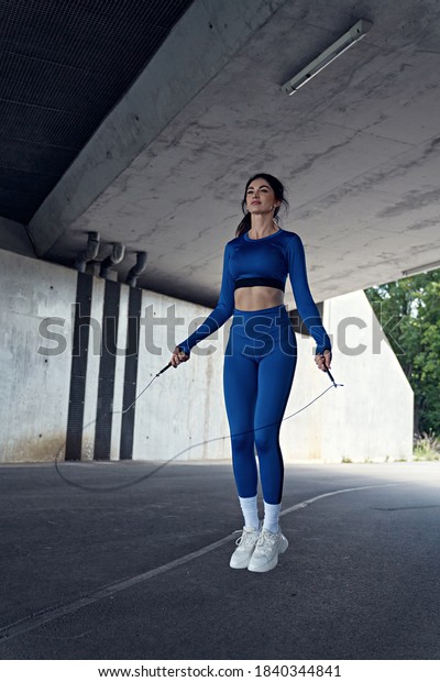 Attractive, athletic woman skipping the rope under\
the urban bridge