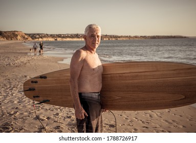 Attractive Australian Mature Man Surfer With Cool Vintage Surfboard On Beach At Sunset. Senior Adult Happy To Be Back To Surf . Outdoors Sports Adventure, Active Older People And Retirement Lifestyle.