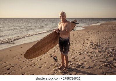 Attractive Australian Mature Man Surfer With Cool Vintage Surfboard On Beach At Sunset. Senior Adult Happy To Be Back To Surf . Outdoors Sports Adventure, Active Older People And Retirement Lifestyle.