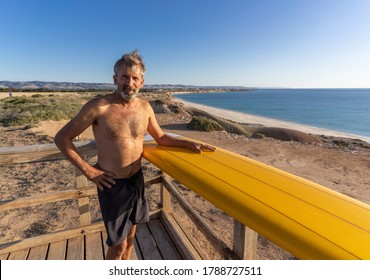 Attractive Australian Mature Man Surfer With Cool Vintage Surfboard On Beach At Sunset. Senior Adult Happy To Be Back To Surf . Outdoors Sports Adventure, Active Older People And Retirement Lifestyle.