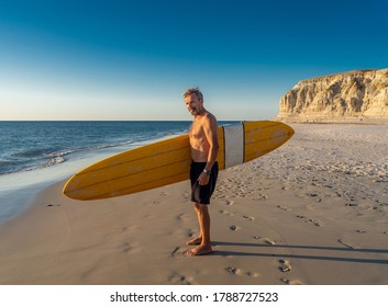 Attractive Australian Mature Man Surfer With Cool Vintage Surfboard On Beach At Sunset. Senior Adult Happy To Be Back To Surf . Outdoors Sports Adventure, Active Older People And Retirement Lifestyle.