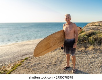 Attractive Australian Mature Man Surfer With Cool Vintage Surfboard On Beach At Sunset. Senior Adult Happy To Be Back To Surf . Outdoors Sports Adventure, Active Older People And Retirement Lifestyle.