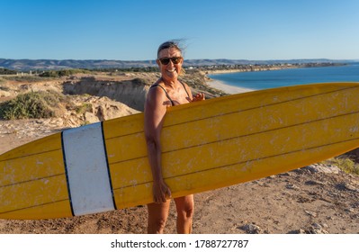 Attractive Australian Mature Surfer With Cool Vintage Surfboard At Sunset. Fit Woman In Her 50s Happy To Be Back To Surf . Outdoors Sports Adventure, Active Older People And Retirement Lifestyle.