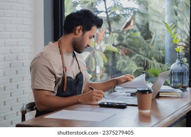 Attractive barista male or employee concentrate on stacks of tax declaration bills, restaurant owner using laptop for bookkeeping control payment, multitask small business lifestyle doing everything - Powered by Shutterstock