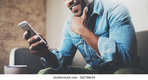 Attractive bearded African businessman using smartphone while sitting on sofa at his home.Concept of young people working mobile devices.Closeup with a selected focus.Blurred background.Wide - Shutterstock ID 562748614