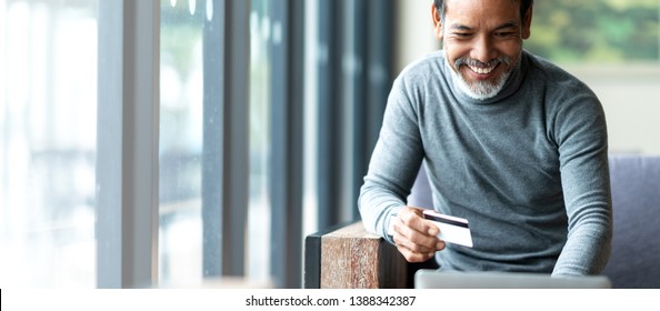 Attractive bearded hipster asian father or Hispanic old man using Laptop and credit card payment shopping online with customer network connection via omni channel system. Older man with technology.