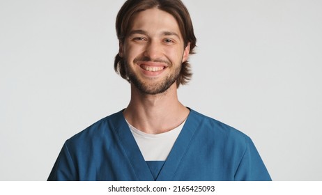 Attractive bearded male doctor smiling at camera against a white background. Beautiful intern dressed in uniform looking happy posing in studio. Medical worker 
