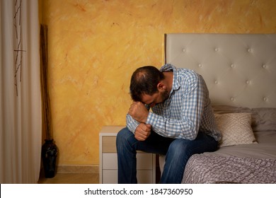 Attractive Bearded Man Depressed And Upset In The Bedroom At Home. Dramatic 30-40 Year Old Lifestyle Portrait, Handsome Man Sitting On Bed, Worried And Desperate. Depression Concept