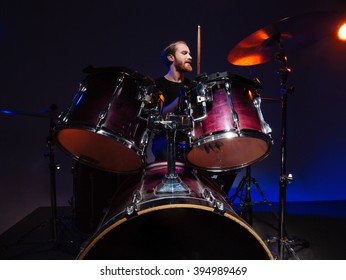 Attractive bearded man drummer sitting and playing on his kit over dark background - Powered by Shutterstock