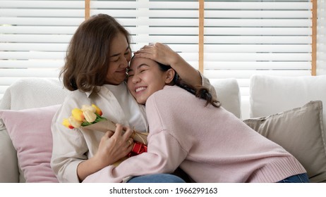 Attractive beautiful asian middle age mum sit with grown up daughter give gift box and flower in family moment celebrate mother day. Overjoy bonding cheerful kid embrace relationship with retired mom. - Shutterstock ID 1966299163