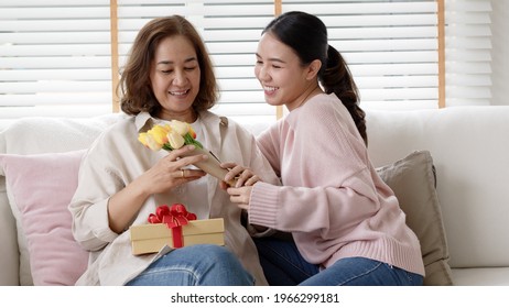 Attractive Beautiful Asian Middle Age Mum Sit With Grown Up Daughter Give Gift Box And Flower In Family Moment Celebrate Mother Day. Overjoy Bonding Cheerful Kid Embrace Relationship With Retired Mom.