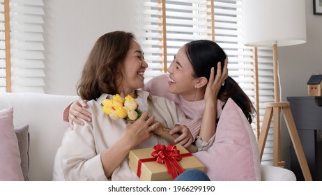 Attractive beautiful asian middle age mum sit with grown up daughter give gift box and flower in family moment celebrate mother day. Overjoy bonding cheerful kid embrace relationship with retired mom. - Shutterstock ID 1966299190