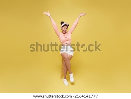 Attractive beautiful Asian teen woman sitting on chair and hands up raised arms success celebration.