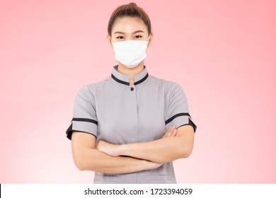 Attractive Beautiful Asian Woman Maid Wearing Face Mask Smile And Cross Arm Feeling So Happiness And Confident,Isolated On Pink Background,Cleaning Service Concept