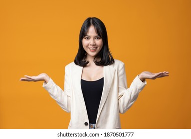 Attractive Beautiful Asian Woman Open Hands Palm Up Holding Something. Sexy Happy Female In Suit On Isolated Yellow Background.