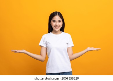 Attractive Beautiful Asian Woman Open Hands Palm Up Holding Something. Surprised Happy Female On Isolated Yellow Background.