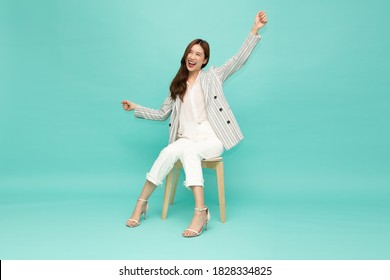 Attractive beautiful Asian woman sitting on white modern chair and hands up raised arms from happiness, Excited businesswoman winner success concept