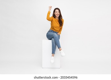 Attractive beautiful Asian woman sitting on white box and hands up raised arms from happiness, Excited female and winner success concept - Shutterstock ID 2033454596