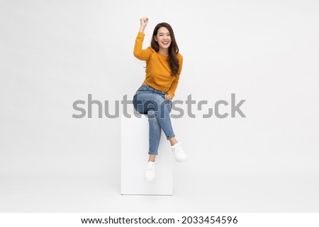 Attractive beautiful Asian woman sitting on white box and hands up raised arms from happiness, Excited female and winner success concept