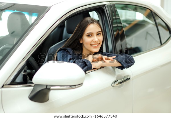 attractive beautiful caucasian woman came to buy new\
automobile in representative dealership. happy lady sit inside of\
car and enjoy it