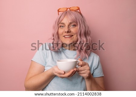 Attractive beautiful female woman hand holds hot cup coffee drink and teapot tea look at camera enjoying sunny morning isolated over pink background.