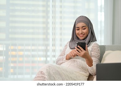 Attractive and beautiful millennial Asian Muslim pregnant woman resting in her home living room, using her mobile phone on the sofa. Motherhood concept - Powered by Shutterstock