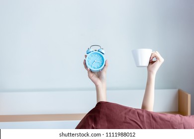 Attractive Beautiful Woman Is Holding Alarm Clock And A Coffee Cup And Raise It To The Air For Showing That It Is A Coffee Time In Morning. Beautiful Girl Love To Drink Coffee In Morning. Copy Space